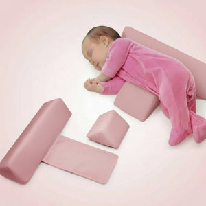 A newborn baby in pink sleepwear lying on a white anti-roll side sleeper pillow with removable cover, alongside a visual representation of the pillow's components.