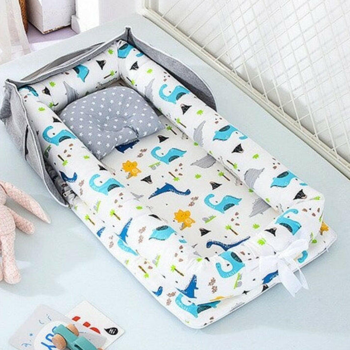 A baby travel sleep bed in pink color, with a woman holding a baby and sitting beside the bed, which appears to be made of cotton fabric. The bed is foldable and has a carry handle, indicating portability.