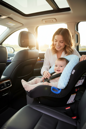 Woman adjusting a baby in a car seat inside a vehicle with a scenic background