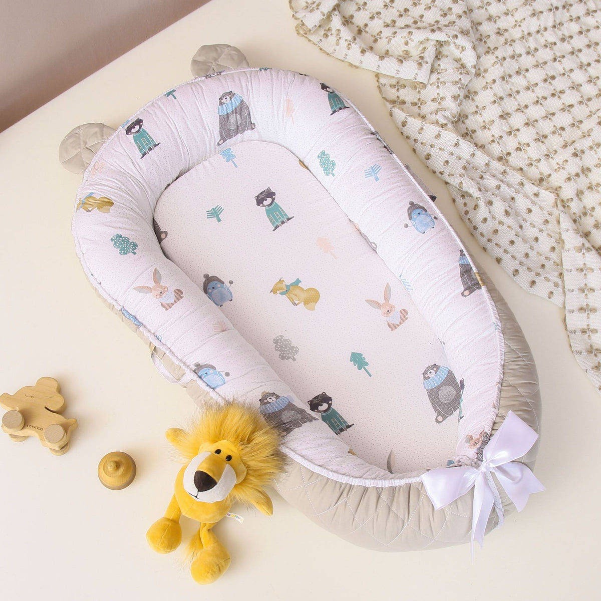 A Cuddle Newborn Baby Lounger with a white fabric covered in a pattern with various baby-themed graphics, including a bear and stars. The lounger is soft, with cushioned edges, and is displayed with a small plush toy and a decorative star beside it.