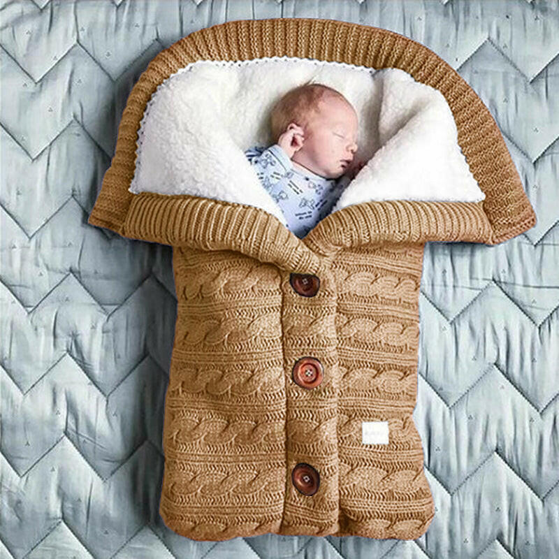 A beige-colored baby sleeping bag with a cable knit pattern, featuring a hood and button closures, with an infant inside.