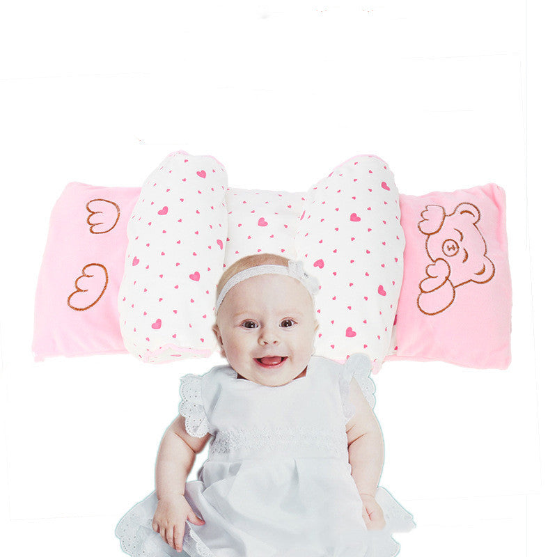 A baby pillow with a plush design featuring different animal faces and the word 'LOVE' on it, with a smiling baby sitting in front of the pillow.