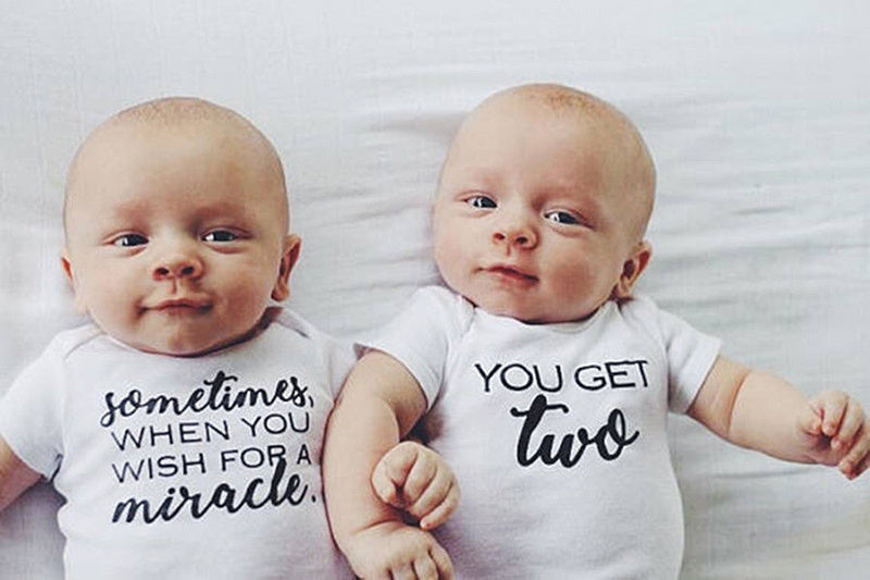Two babies wearing matching onesies with text on a white background