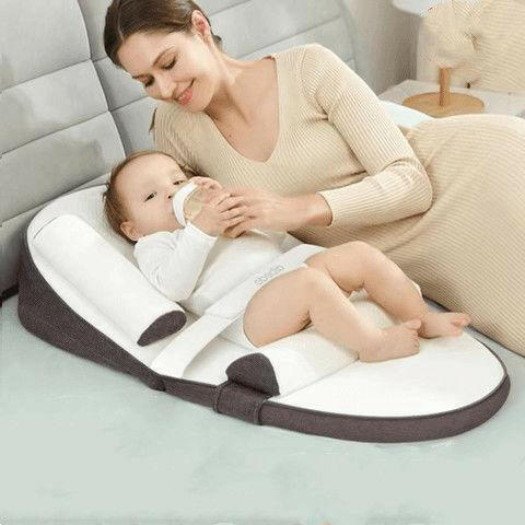 A baby lying on a green and white anti-reflux and anti-roll baby lounger bed.