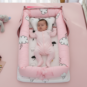Baby lying in a pink crib with cloud patterns on a pink blanket.