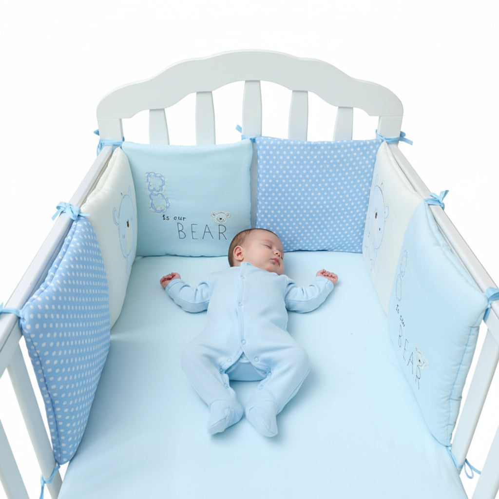 Baby crib with blue crib bumper and pillow set on a white background