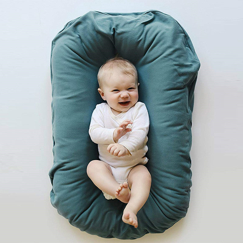 Baby lying on a teal cushion with a plain background
