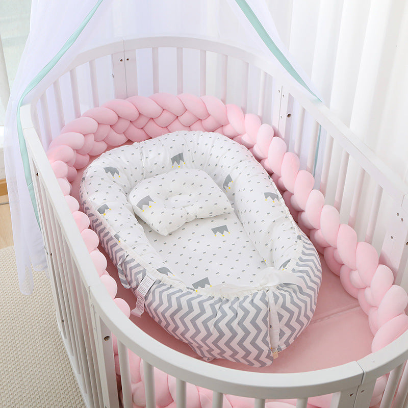 Baby crib with pink bumper and white crib sheet with gray patterns
