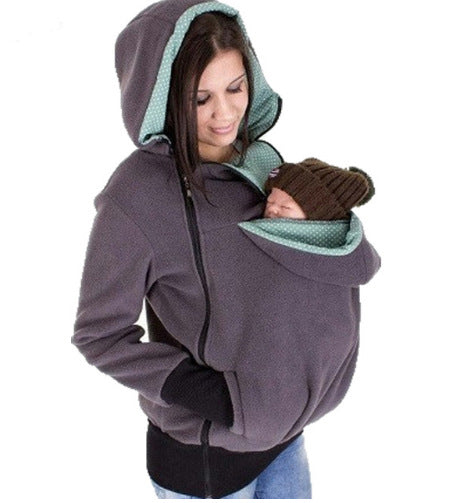Woman wearing a gray hoodie with green lining, holding a baby in a sling.