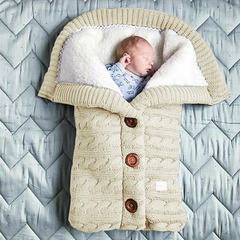 A beige-colored baby sleeping bag with a cable knit pattern, featuring a hood and button closures, with an infant inside.