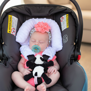 Baby in a car seat with a pacifier and toy, wearing a floral headband.