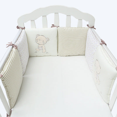 Crib with white bedding and decorative pillows featuring a bear design.