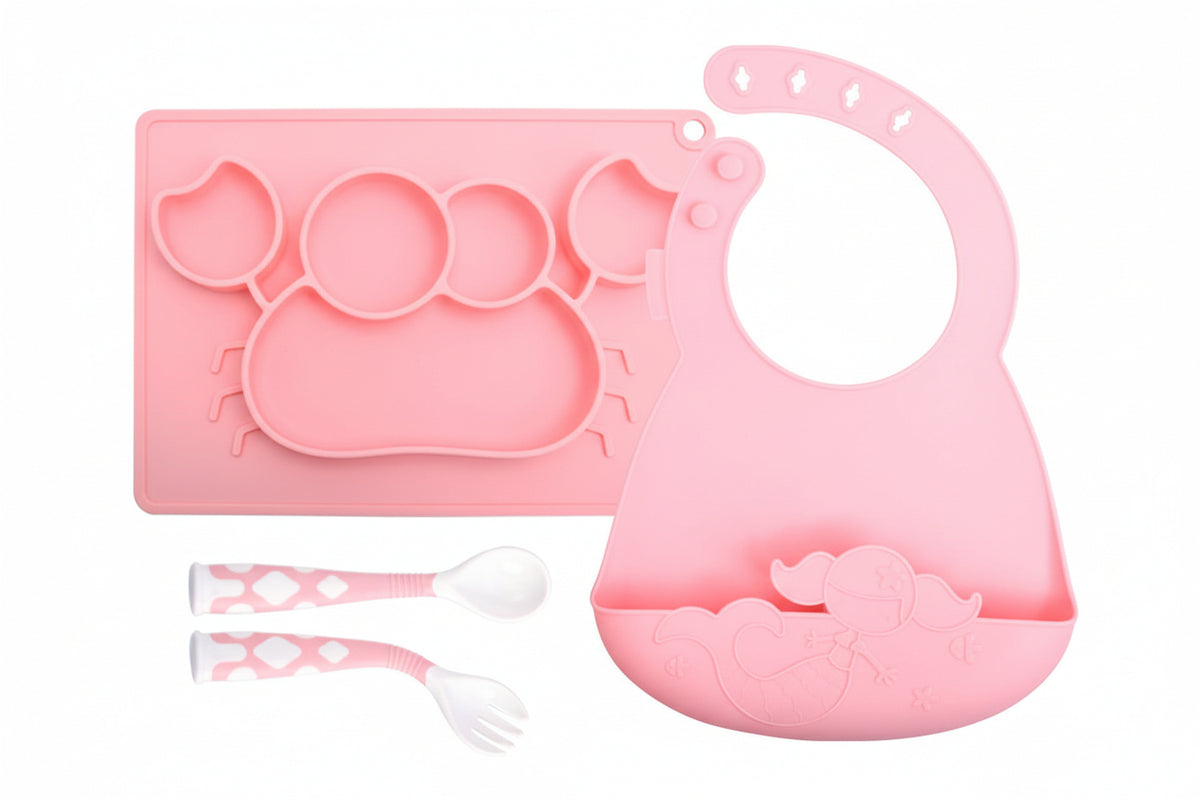 Pink silicone baby plate, bib, spoon, and fork set on a white background