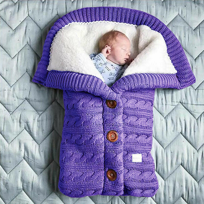A beige-colored baby sleeping bag with a cable knit pattern, featuring a hood and button closures, with an infant inside.