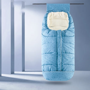 A light blue padded baby sleeping bag with a subtle dotted pattern and a cream-colored inner lining, shown hanging against a minimalist gray studio background.