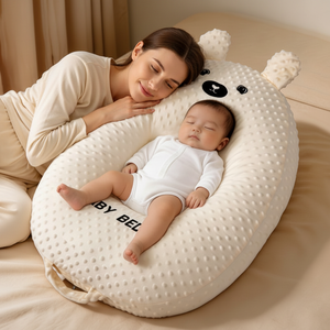 Woman and baby lying on a large white bear-shaped pillow with 'BY BEL' branding.