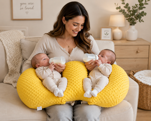 Woman holding two babies on a yellow cushion in a cozy living room.