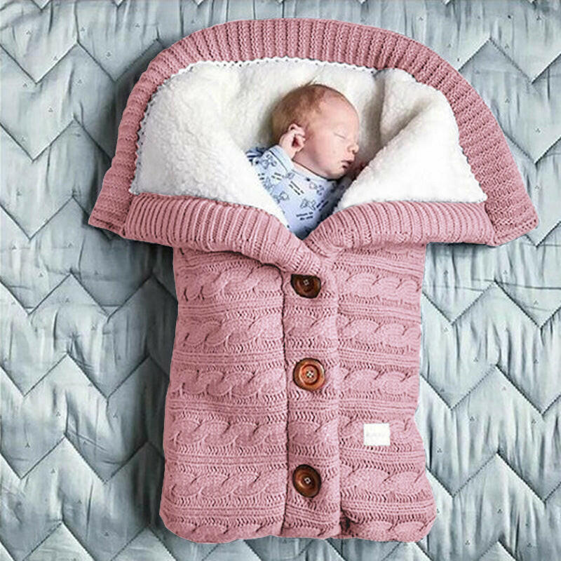 A beige-colored baby sleeping bag with a cable knit pattern, featuring a hood and button closures, with an infant inside.