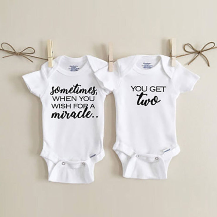 Two white baby onesies with text on a beige background
