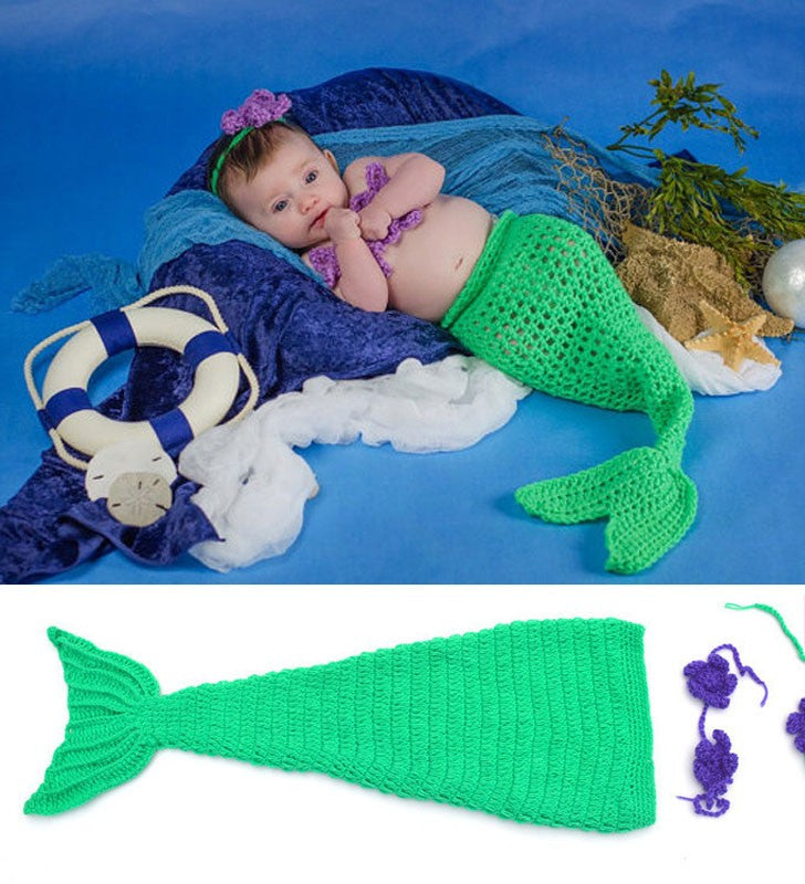 Baby in a green mermaid tail costume on a blue background with sea-themed props.