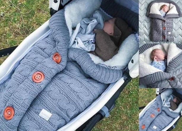 A beige-colored baby sleeping bag with a cable knit pattern, featuring a hood and button closures, with an infant inside.