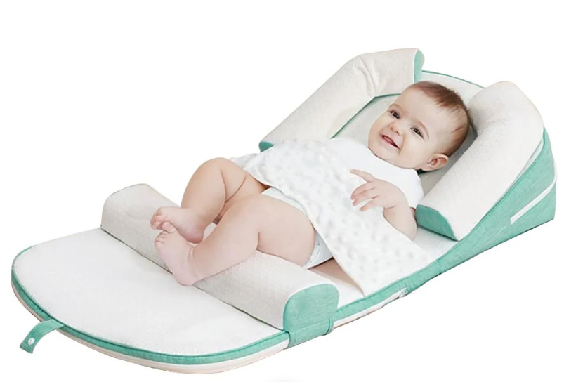 A baby lying on a green and white anti-reflux and anti-roll baby lounger bed.
