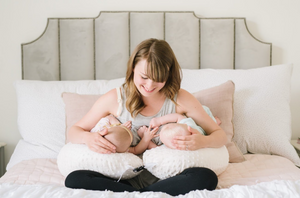 Woman breastfeeding a baby on a bed with a neutral headboard.