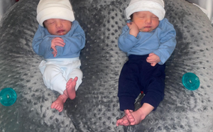 Two newborn babies lying on a textured surface with blue and white clothing.