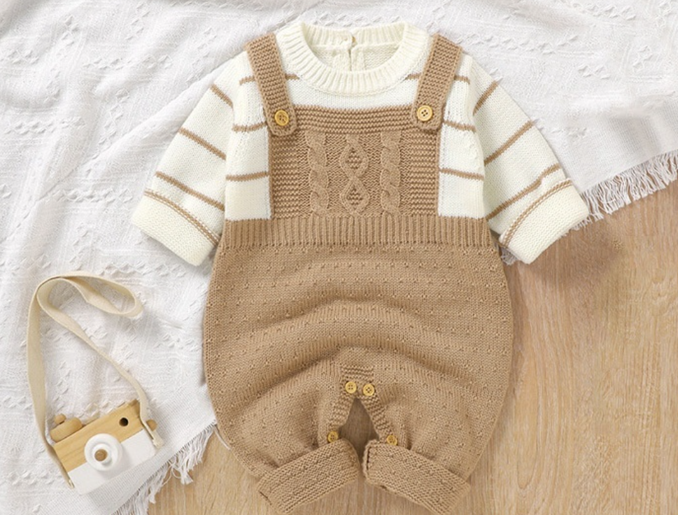 Baby outfit with beige knitted overalls and striped shirt on a light wooden surface.