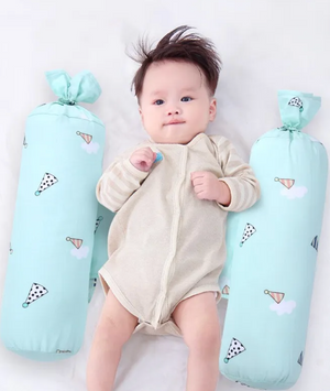 Baby lying between two light blue pillows with cloud patterns on a white background