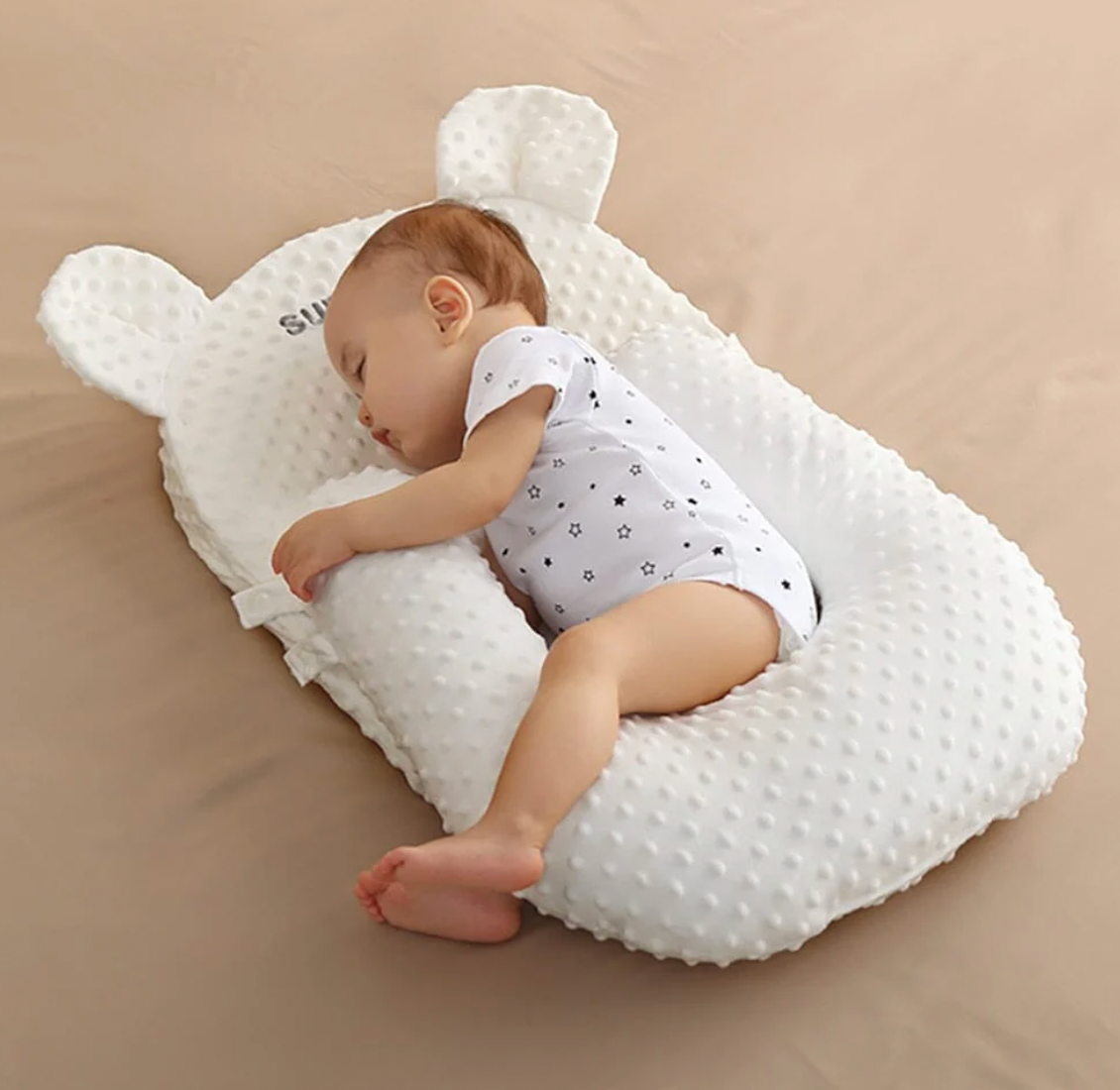Baby sleeping on a white pillow with bear ears on a beige surface