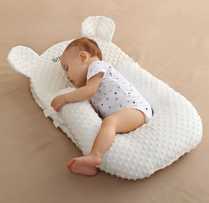 Baby sleeping on a white pillow with bear ears on a beige surface