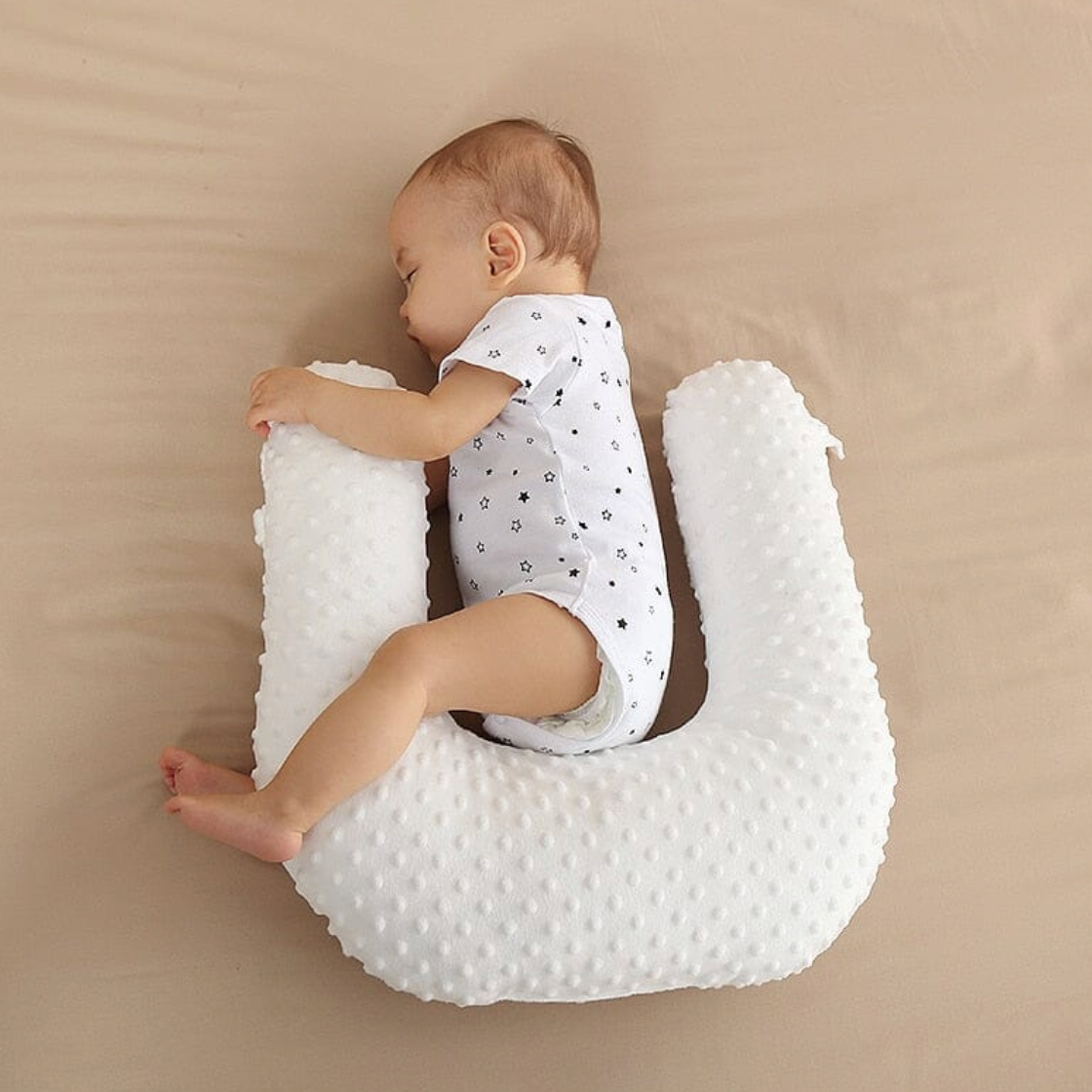 Baby sitting on a white U-shaped pillow against a beige background