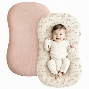 Baby lying on a floral-patterned cushion next to a pink cushion on a white background