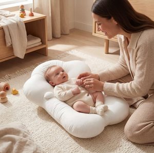 Woman sitting on the floor with a baby in a white baby seat in a bright room.