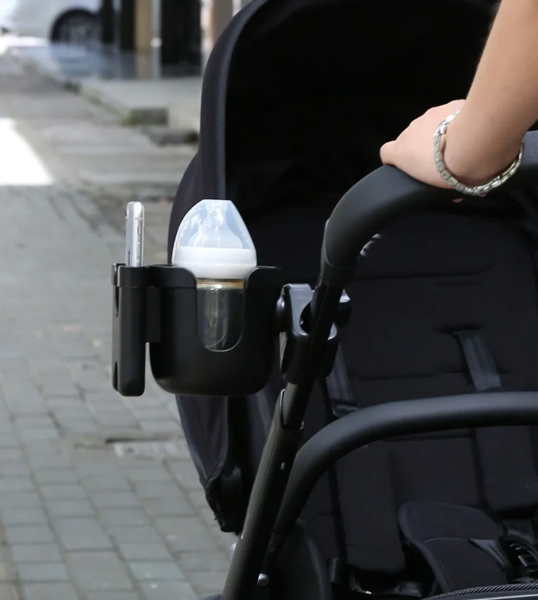 Baby bottle holder attached to a stroller on a sidewalk