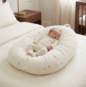 Baby sleeping in a white crib bumper in a bedroom setting.