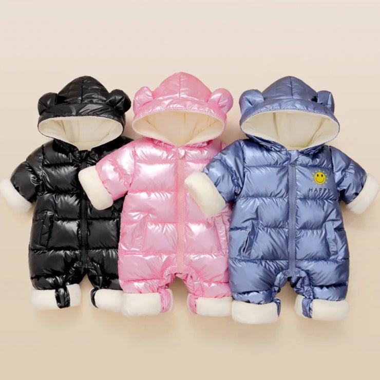 Three baby snowsuits in black, pink, and blue on a beige background