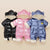 Three baby snowsuits in black, pink, and blue on a beige background