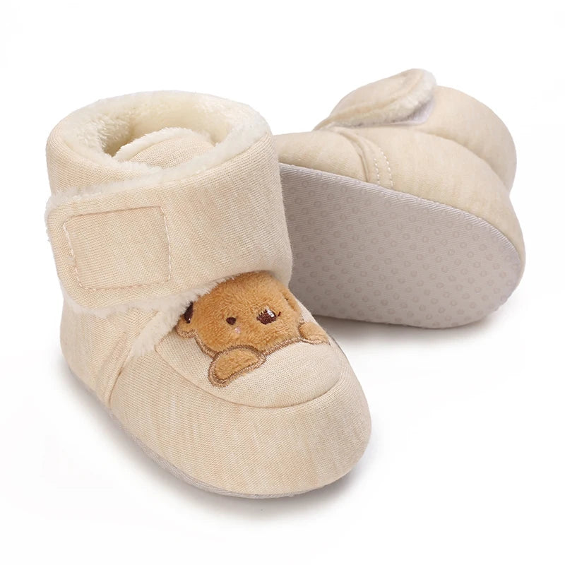 Beige baby booties with a teddy bear design on a white background