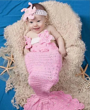 Baby in a pink mermaid costume sitting on a textured surface with starfish decorations.