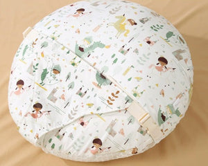 A round, quilted baby support pillow with a white background and a colorful cartoon dinosaur and child pattern, shown on a beige fabric background with a Chinese text label in the top right corner.