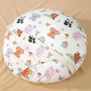 A round baby cushion cover featuring a colorful cartoon animal print, including bears, pandas, bunnies, and houses on a cream background. It is shown folded on a beige fabric surface 