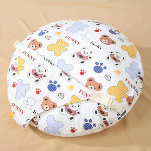 A round baby nursing pillow with a white background and a colorful cartoon bear print, featuring a beige strap with a plastic buckle. The image is set against a soft beige background 