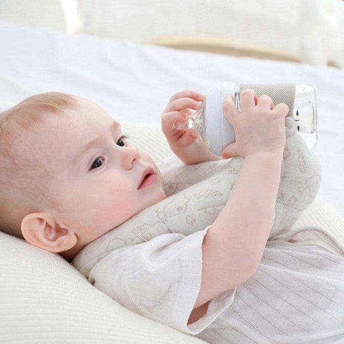 A baby lying on a hands-free self-feeding pillow, holding a bottle.