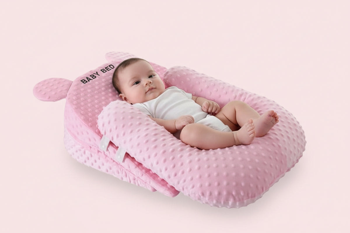Pink baby nest with 'BABY BED' branding on a light gray background