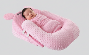 Newborn baby sleeping in a pink minky dot baby nest on a light gray background