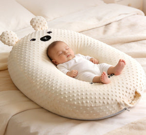 Baby sleeping in a large, plush, white bear-shaped pillow on a bed.