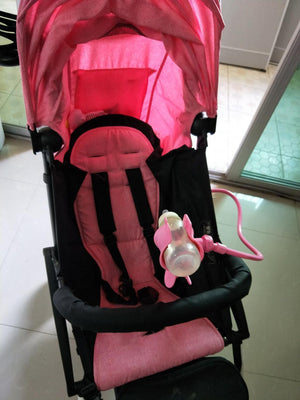 Pink and black stroller with a pink toy on a tiled floor.