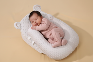 Newborn baby in a pink outfit sleeping in a white crib on a beige background